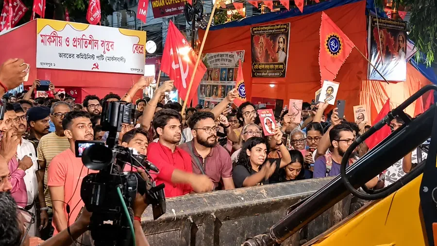 A crowd gathers outside a CPIM book stall in Jadavpur, Kolkata as a bulldozer stands in the foreground amid a dispute over the stall during Durga Puja.