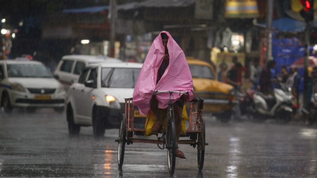 A commuter covers himself with tarpaulin amid heavy rain , in Kolkata