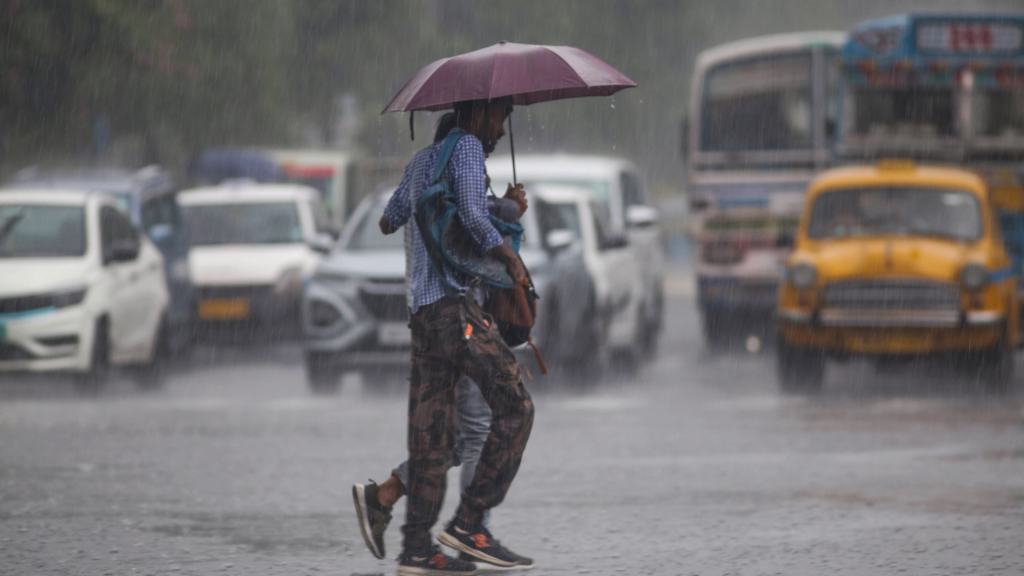 People cross a rain-soaked Kolkata road under an umbrella during heavy rainfall.