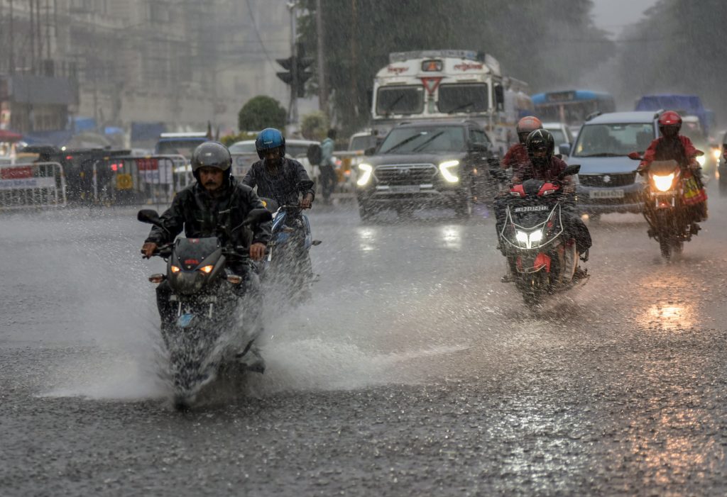 Motorcyclists ride through a rain-soaked Kolkata street during heavy rainfall.