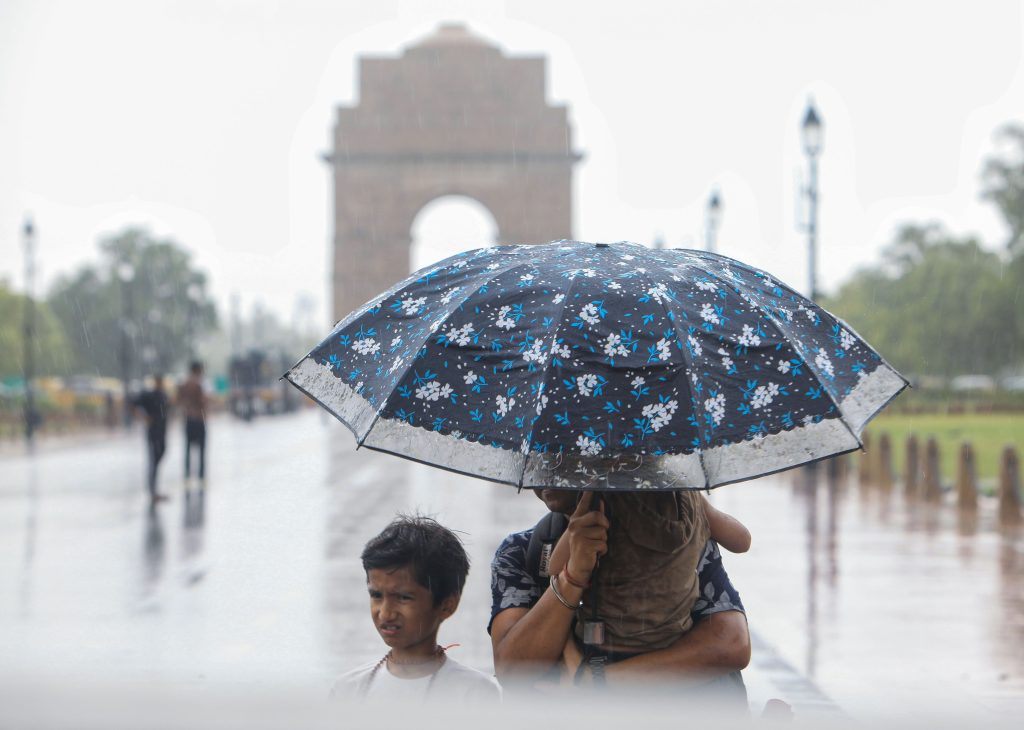 Family shelters under umbrella near India Gate in Delhi rain.
