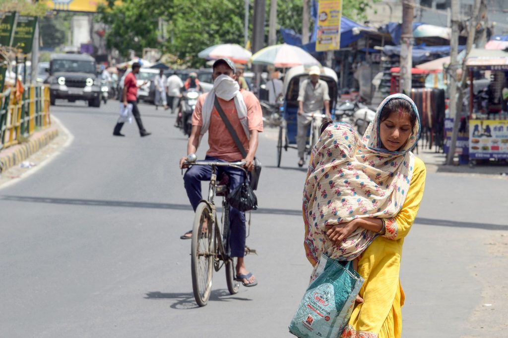 A woman covering herself and a child in her arms with a stole, walks on a road amid the scorching sun and heatwaves, in Jalandhar | File image/ANI