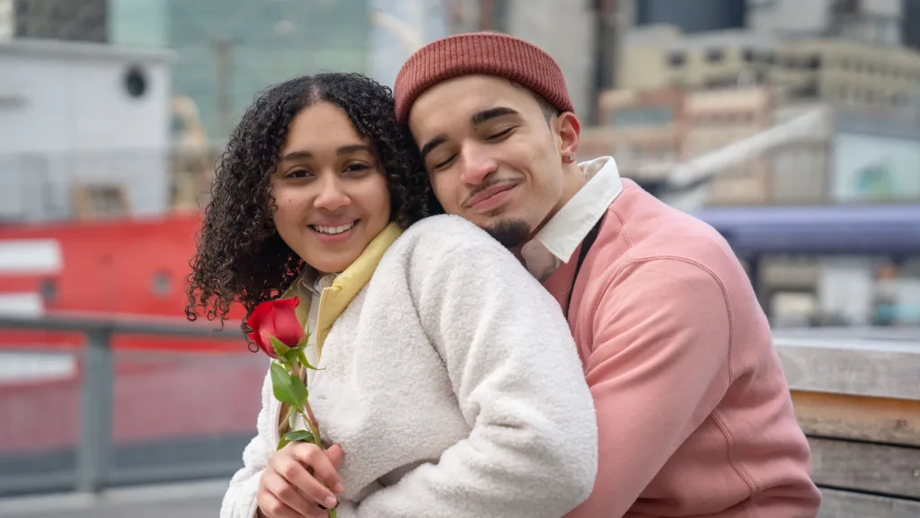 Smiling couple enjoying a warm embrace with a rose in an urban setting, exuding love and connection