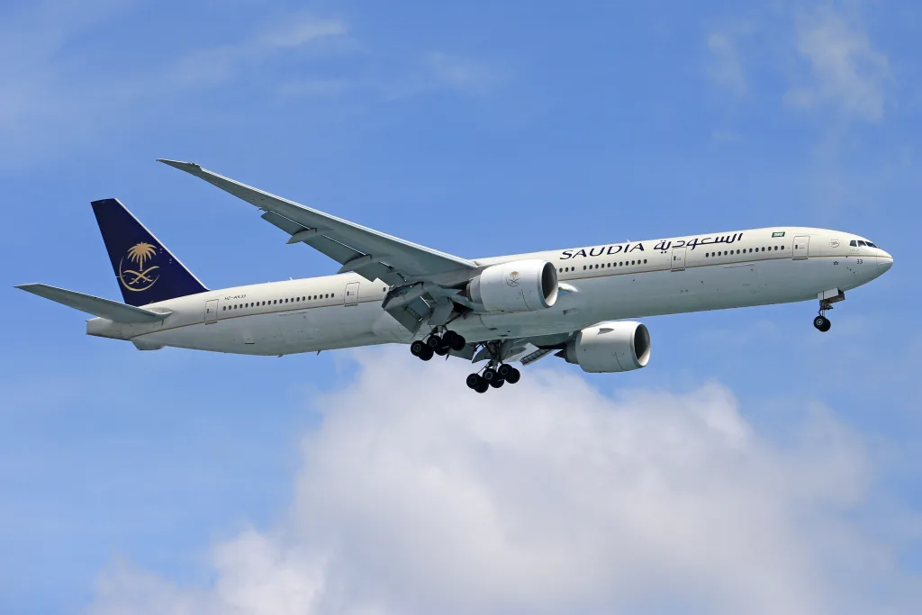 Saudia Airlines aircraft flying high in a clear blue sky