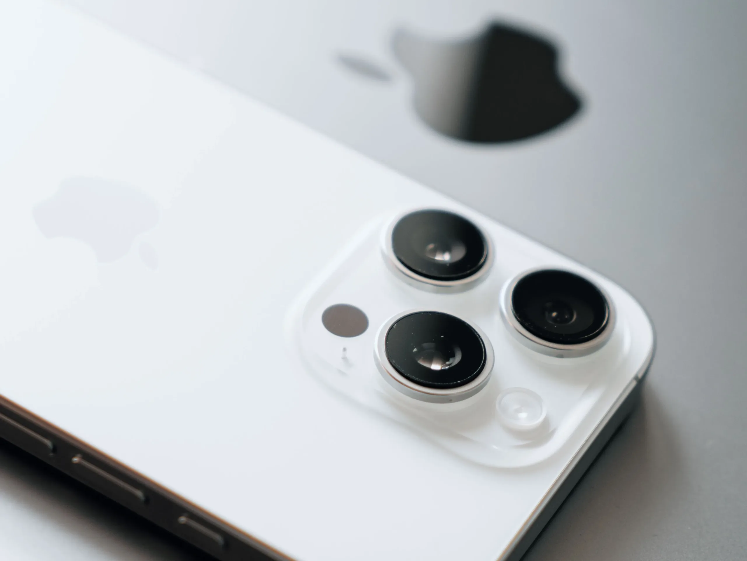 White iPhone with triple cameras lies atop a sleek laptop.