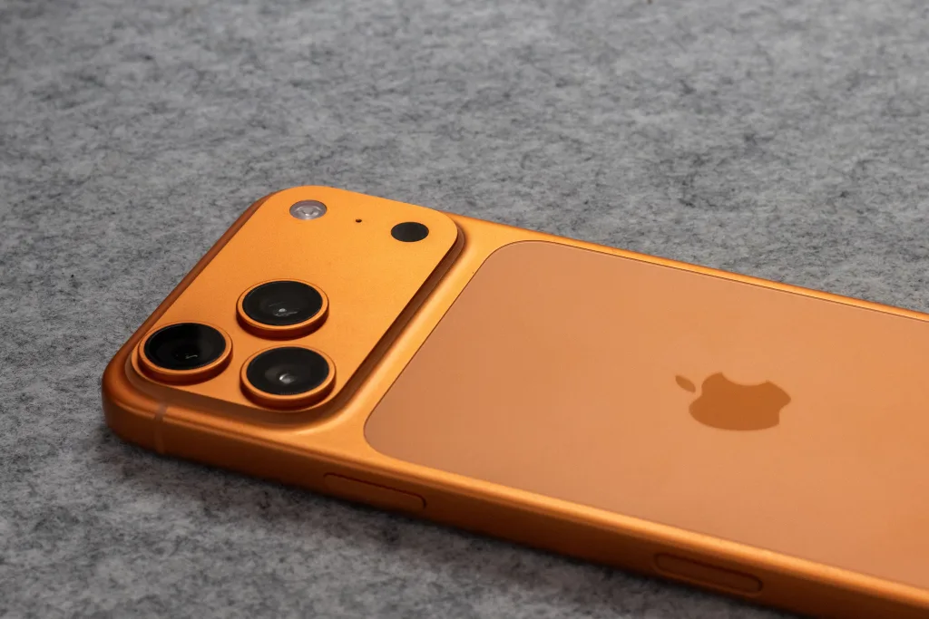 Orange smartphone with dual cameras placed on a soft gray fabric surface / Pexels