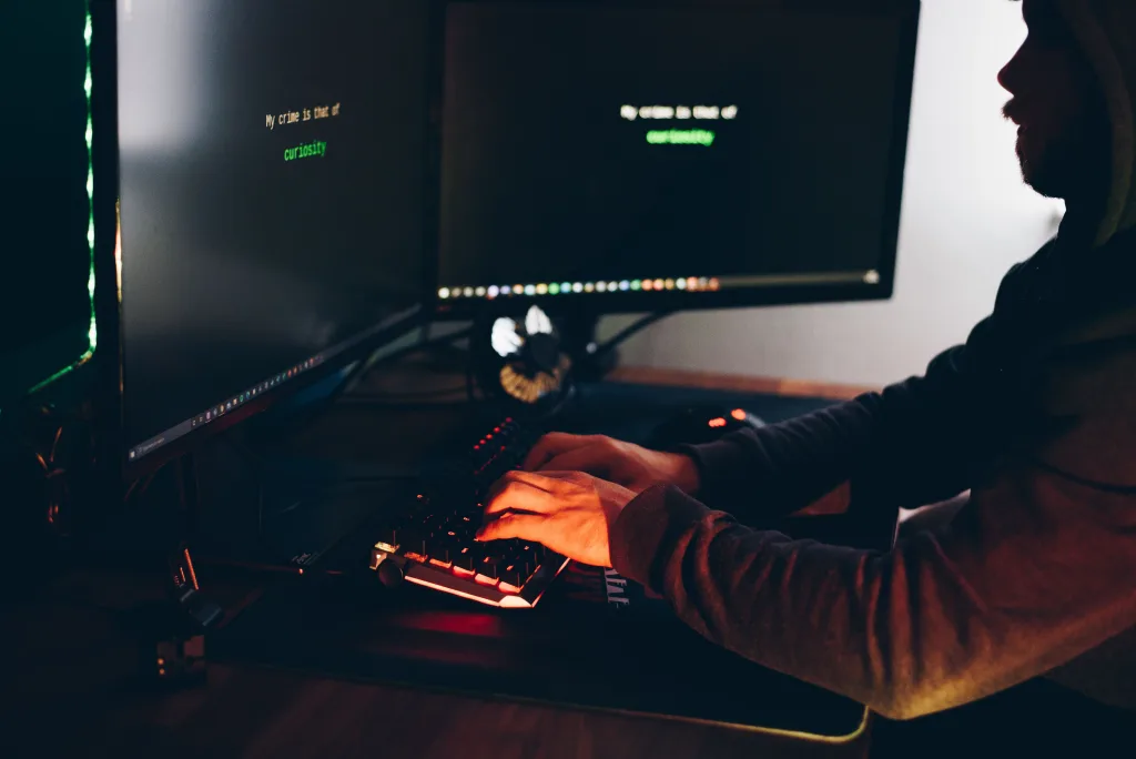 Silhouette of a person typing on a computer in a dimly lit room, emphasizing cybersecurity threats